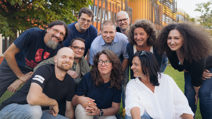 plan2net Team am Campus der WU Wien, eine Gruppe von 10 Personen hockerlt auf einer Wiese, sie lachen und freuen sich
