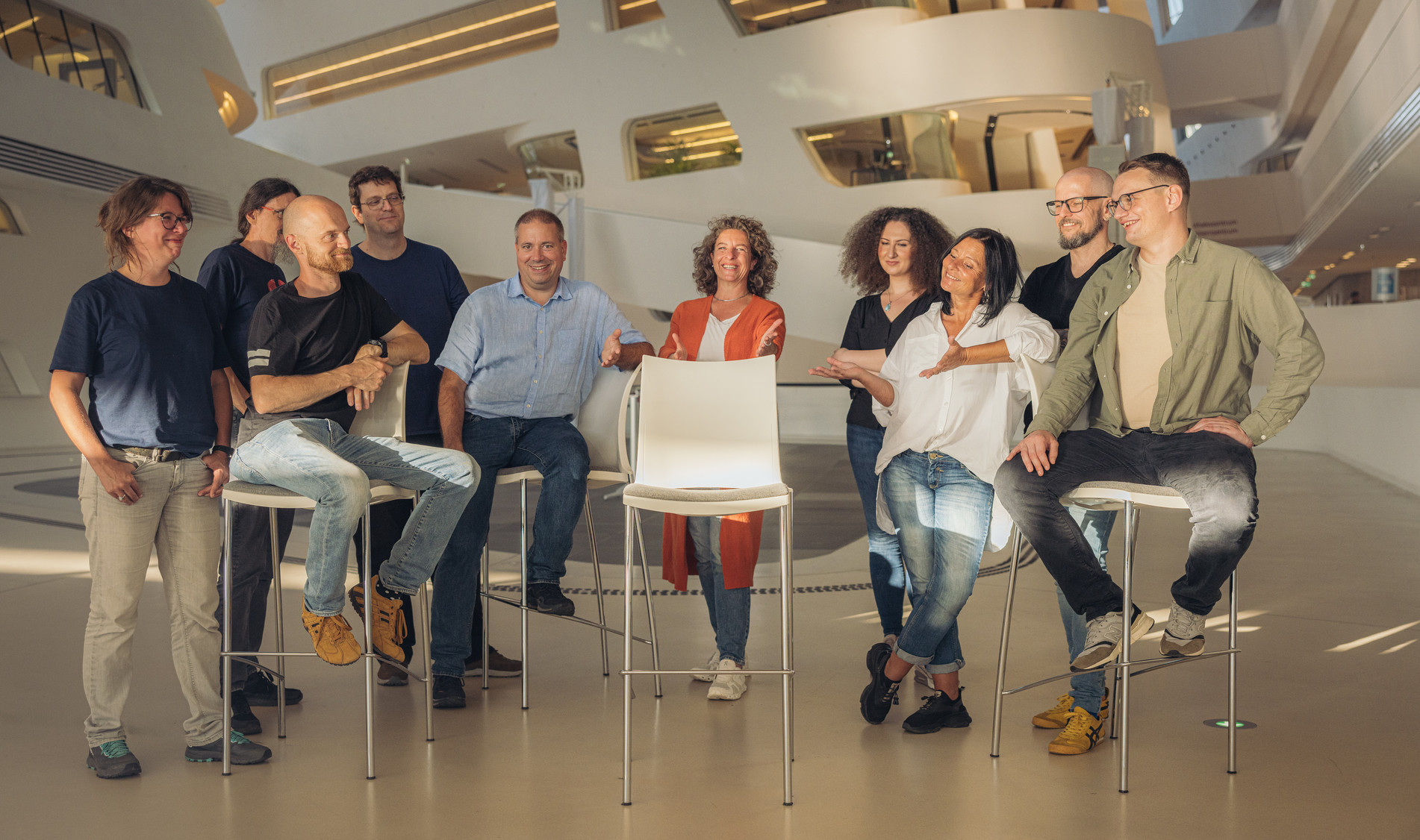Team lädt ein zum Platz nehmen, Sessel in der Mitte ist frei